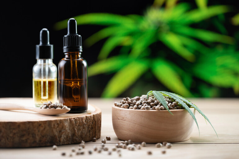 CBD tinctures with hemp seeds and bottles on a wooden surface, with a cannabis plant in the background