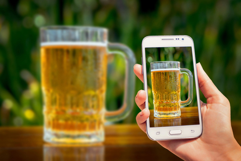 Taking pictures of homebrews using a smartphone, highlighting technology's impact on the beer scene