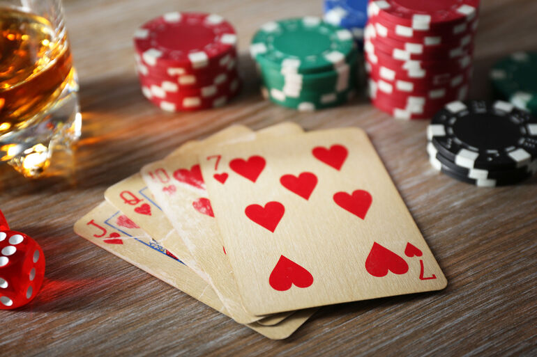 A beer glass, cards, and casino chips on a wooden table