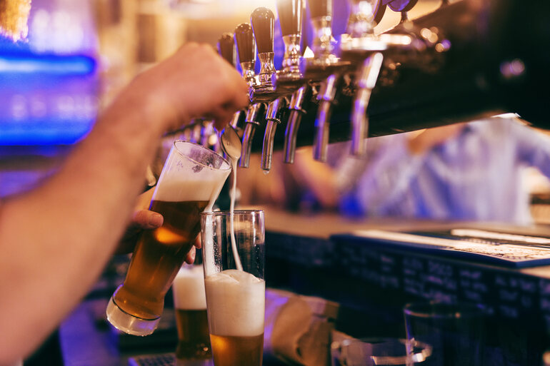 Bartender pouring a glass of beer from a tap in a brewery setting.