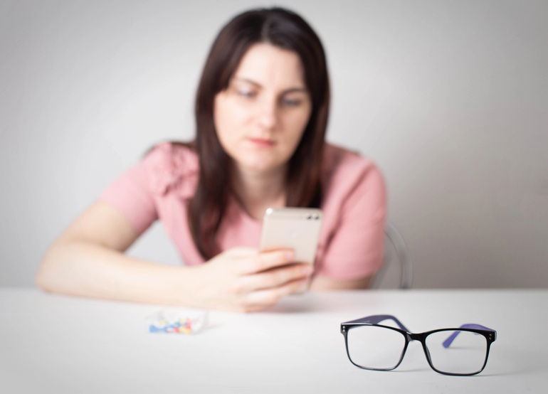 A girl looks at the smartphone screen and glasses placed on the table