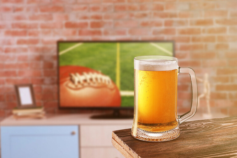Glass of homemade beer on the table with the TV screen in the background