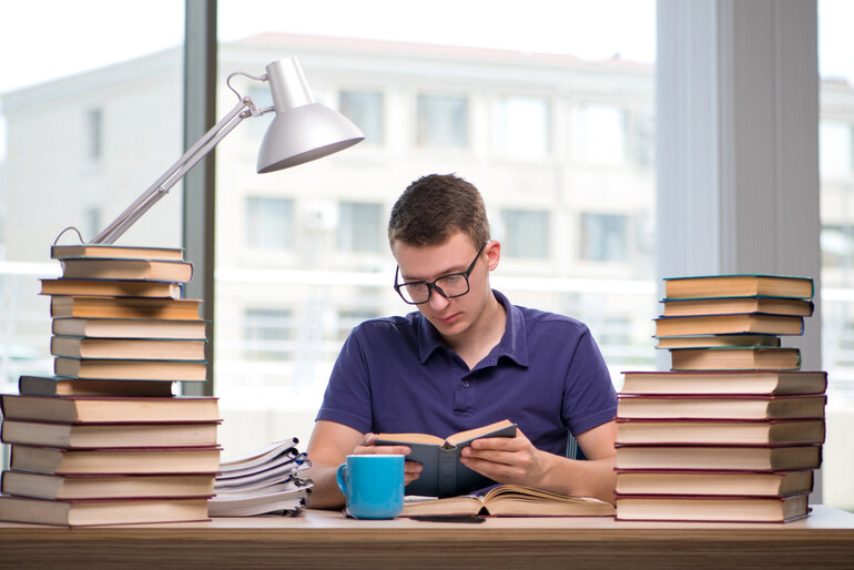 A Focused student surrounded by books, studying with a coffee mug on the desk