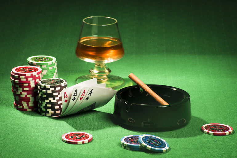 A glass of beer, a cigar in a black ashtray, poker chips, and a winning hand of four aces on a green casino table