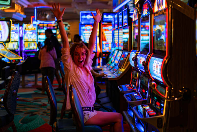 A girl celebrating a win while sitting in front of a slot machine in a casino